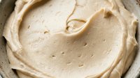 Creamy beige spread with swirled texture in bowl, suitable for food photography, culinary content, recipe blogs, and ingredient close-ups.