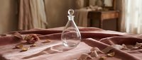 Empty glass perfume bottle with stopper placed on crumpled mauve fabric, soft natural lighting, suitable for fragrance packaging design and cosmetic advertising.