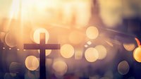 Christian cross silhouette against golden sunset sky with soft bokeh lights creating spiritual atmosphere. Religious symbol of faith and hope.