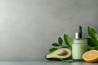 Green cosmetic bottle with dropper near fresh avocado, citrus and tropical leaves on gray background. Natural skincare and beauty concept.