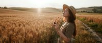 Woman farmer in straw hat standing in golden wheat field at sunset, holding grain stalks, agricultural work and harvest season.