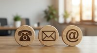 Wooden contact icons on desk showing phone, email and at symbol for business communication and customer service in modern office environment.