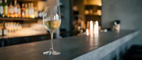 Glass of white wine on elegant bar counter with blurred restaurant background creating sophisticated dining atmosphere for hospitality marketing.