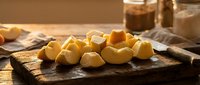 Fresh yellow cheese cubes on rustic wooden cutting board with knife, warm kitchen lighting for culinary cooking and food preparation concepts.