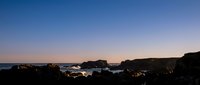 Dramatic coastal landscape at twilight with rocky cliffs and ocean waves under purple and orange sunset sky creating serene seascape atmosphere.