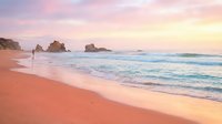 Serene coastal landscape at sunrise with soft pink sand, gentle waves, and distant rock formations, perfect for travel and nature backgrounds.