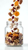 Mixed nuts and dried fruits falling into glass jar on white background, including cashews, pecans, walnuts, apricots and cranberries for healthy snacking and nutrition.
