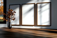 Three empty wooden frames on gray wall with natural light shadow and decorative orange autumn leaves in vase, modern minimalist interior design.