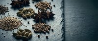 Aromatic spices and seeds scattered on dark slate surface including star anise, cardamom pods, coriander and peppercorns for culinary cooking.