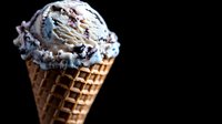 Creamy cookies and cream ice cream scoop in crispy waffle cone against dark background, showcasing rich texture and swirls of vanilla and chocolate cookie pieces.
