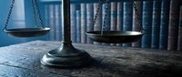 Vintage brass scales of justice on wooden desk with law books in background, legal concept for courtroom attorney lawyer judicial system.