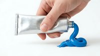 Hand squeezing blue acrylic paint from silver tube onto white surface for art projects and creative painting activities.