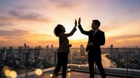 Silhouettes of two business professionals giving high five on rooftop at sunset with city skyline in background, celebrating success and teamwork in corporate environment.