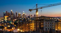 Urban construction site with tower crane building residential complex at sunset with city skyline backdrop for real estate development projects.