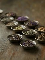 Aromatic dried herbs and tea leaves displayed in rustic ceramic bowls on dark wooden surface, moody natural lighting creates depth and texture for culinary design.