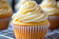 Vanilla cupcake topped with swirled buttercream frosting and white pearl sprinkles on cooling rack, macro food photography with soft natural lighting.