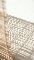 Natural bamboo fence casting geometric shadow patterns on white wall creating minimalist zen atmosphere for interior design and architecture projects.