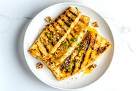 Grilled halloumi cheese slices with herbs and honey drizzle on white plate against marble background, golden char marks and melting texture.
