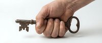 Male hand holding vintage rusty metal key on white background, isolated antique object for security, access, mystery and unlocking concepts.