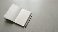 Open blank notebook with white pages and black pen on gray textured surface for writing, journaling, planning, and creative projects.