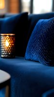 Cozy evening atmosphere with navy blue velvet sofa cushions and glowing candlelight in decorative metal holder creating warm ambient lighting for relaxation.