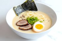 Traditional creamy tonkotsu ramen bowl with tender chashu pork, soft-boiled egg, nori seaweed, green onions and thin noodles in rich pork bone broth.