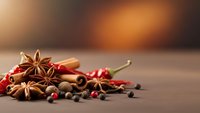 Aromatic spices including star anise, cinnamon sticks, red chili peppers and peppercorns arranged on wooden surface for culinary cooking and seasoning.