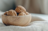 Fresh whole walnuts in wooden bowl on white linen fabric. Natural organic nuts for healthy eating, cooking and snacking concepts.
