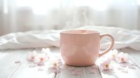 Steaming pink cup of hot tea or coffee on a wooden table with cherry blossom flowers in a cozy morning atmosphere.