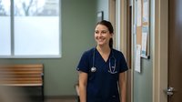 Young female healthcare professional with South Asian ethnicity wearing navy scrubs and stethoscope in clinical office setting, suitable for medical, nursing, and healthcare industry marketing materials.
