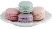 Colorful French macarons in pastel mint, pink, purple, and peach shades arranged on white porcelain plate, isolated on white background for food photography and design.