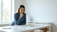 Professional businesswoman in blue suit analyzing financial charts and graphs at modern office desk near window for corporate strategy planning.