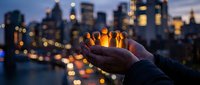 Young adult male holding glowing orb of light against illuminated city skyline at dusk, representing innovation, ideas, and urban energy for business and technology concepts.