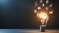 Glowing light bulb with brain inside surrounded by floating energy and technology icons on dark blue background for innovation concepts.