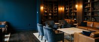 Elegant upscale restaurant interior with blue velvet chairs, wooden bookshelves, warm lighting and modern dining tables for hospitality design.