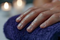 Female hand with natural manicure resting on purple spa towel, soft candlelight creates relaxing atmosphere for wellness and beauty treatments.