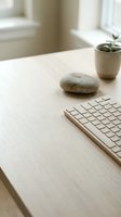 Minimalist workspace with wireless keyboard, smooth stone, and potted succulent on light wooden desk near bright window for modern office design projects.