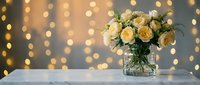 Fresh yellow roses in glass vase on marble surface with warm golden bokeh lights background for romantic occasions and home decor.