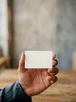 Hand holding blank white business card with blurred interior background, suitable for branding, corporate identity, and professional mockup designs.