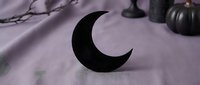 Black crescent moon symbol on purple fabric with candles and branches creating mystical witchcraft altar setup for spiritual rituals and magic practices.