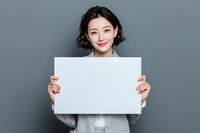 Young Asian businesswoman with short curly hair holding blank white sign against gray background, perfect for adding custom message or advertisement.