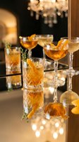 Elegant amber cocktails with orange garnish on reflective bar surface in upscale lounge with warm chandelier lighting creating luxurious evening atmosphere.