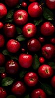 Fresh red apples and small cherries scattered on dark background with green leaves. Water drops add shine to fruit surface. Dramatic food photography for healthy eating concept.