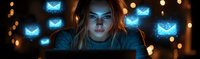 Young woman illuminated by blue light from laptop screen with glowing email icons floating around her, depicting digital communication and night work environment.