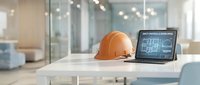 Orange safety helmet and laptop displaying architectural blueprints on modern office desk. Construction planning and engineering workspace concept.