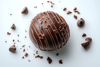 Round chocolate truffle with drizzled milk chocolate lines and sprinkled cocoa nibs scattered around on white background, isolated confectionery dessert for food photography.