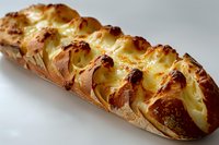 Freshly baked braided bread filled with sweet cream cheese and topped with golden-brown crust, photographed in natural light against white background.