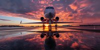 Luxury private jet reflected in wet runway during dramatic sunset with vibrant orange and purple sky, perfect for aviation, travel and business concepts.