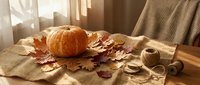 Autumn home decor with orange pumpkin and dried leaves on rustic burlap fabric in warm sunlight for seasonal interior design and fall decorating.