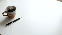 Minimalist workspace with coffee cup and pen on clean white desk surface for productivity and creative writing projects.